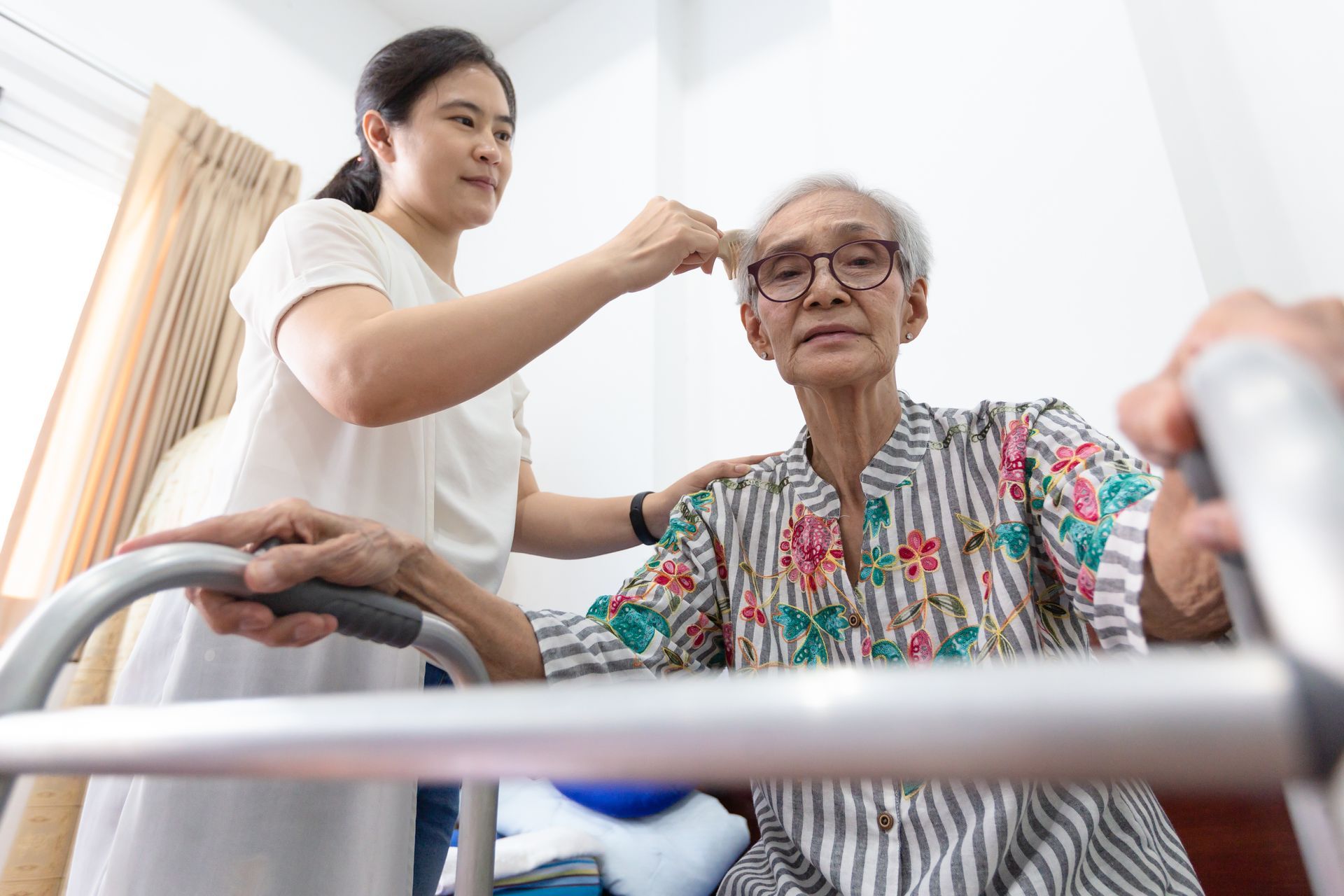 Woman assists an elderly woman using a walker, adjusting her hair. Indoor, daytime.