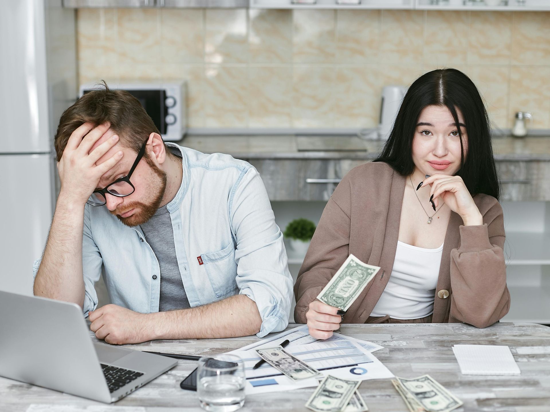 Frustrated couple at a table with bills and laptop, suggesting financial stress