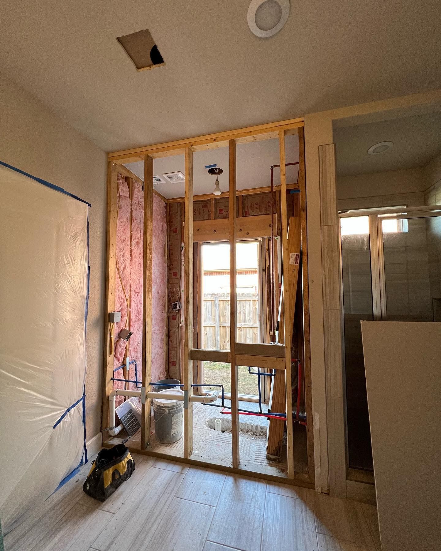 Bathroom under construction; framing, insulation, plumbing visible; unfinished walls, light flooring.