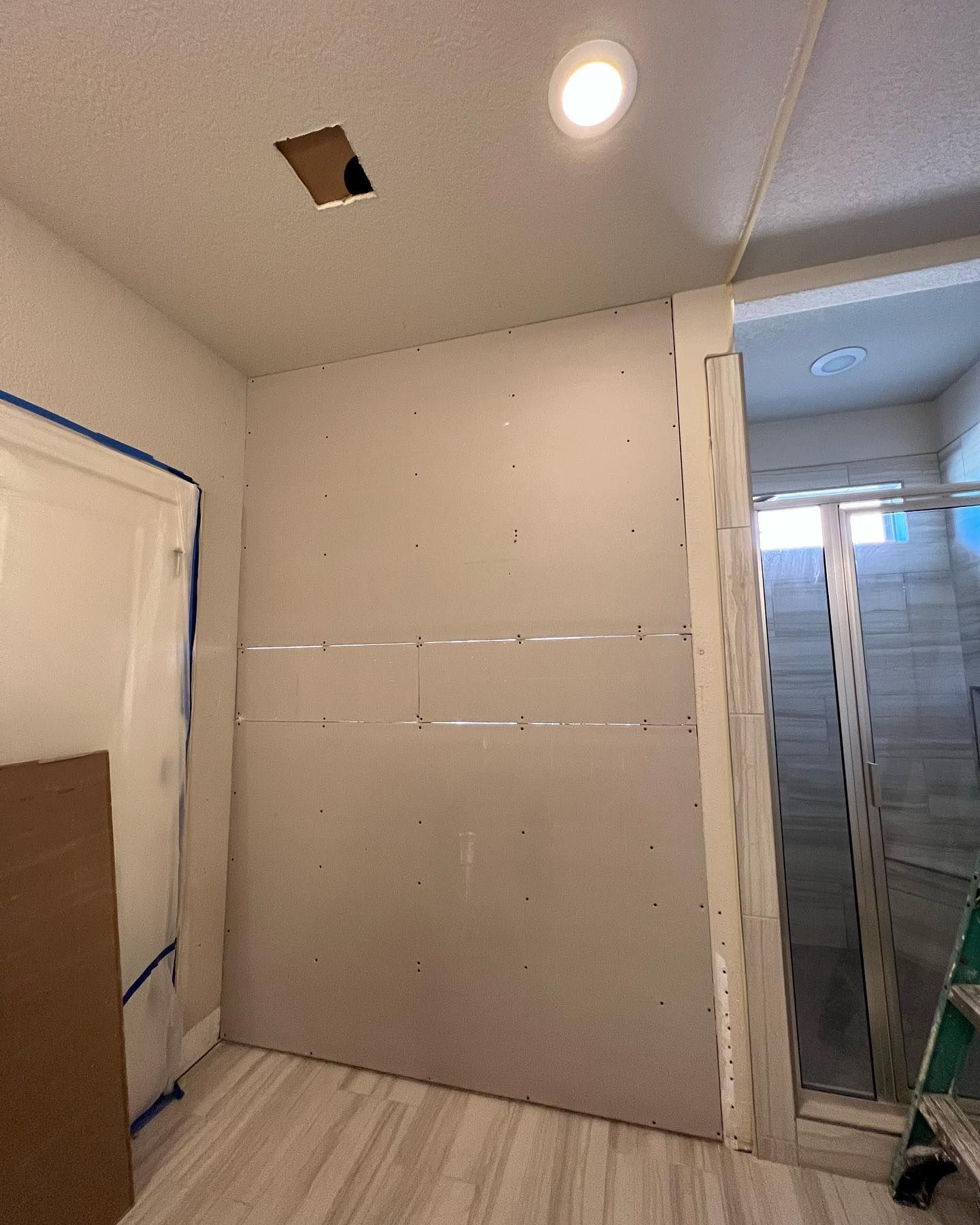 Bathroom renovation in progress; drywall on walls, doorframe, and unfinished ceiling with recessed light.