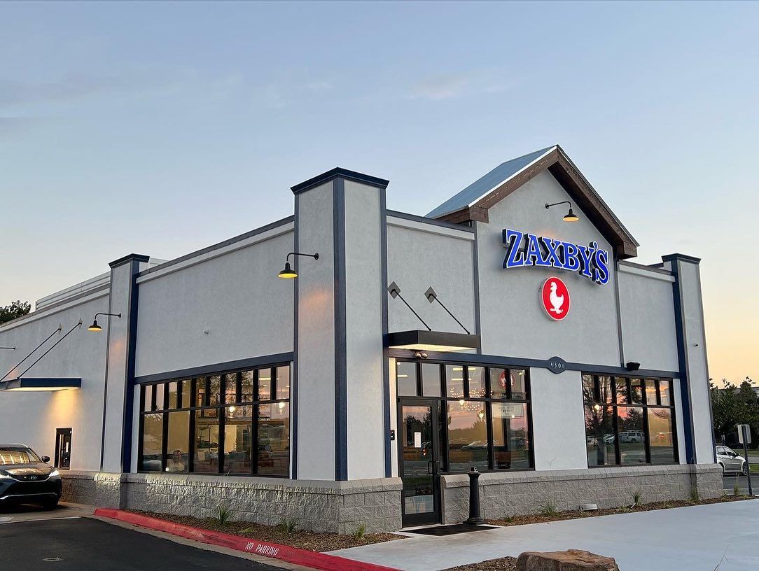 Exterior of a Zaxby's restaurant with white walls, blue trim, and a red chicken logo.