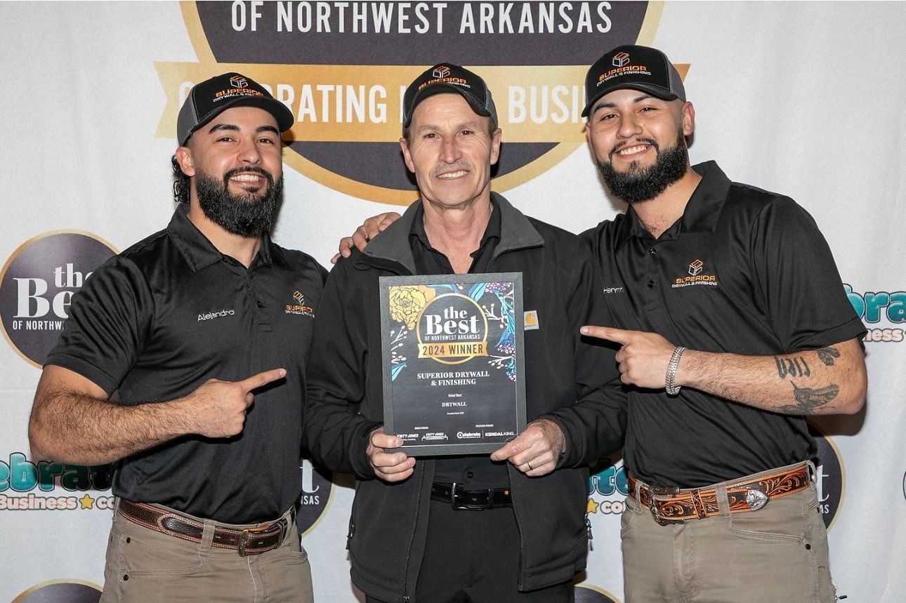 Three men holding award, pointing. One in middle holds the award, two on sides pointing.