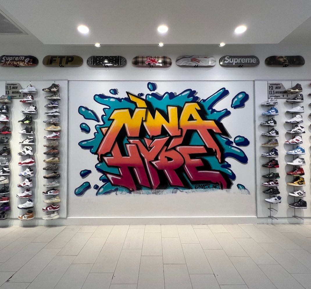 Sneaker store interior with graffiti art and display shelves of shoes. Skateboards line the upper wall.