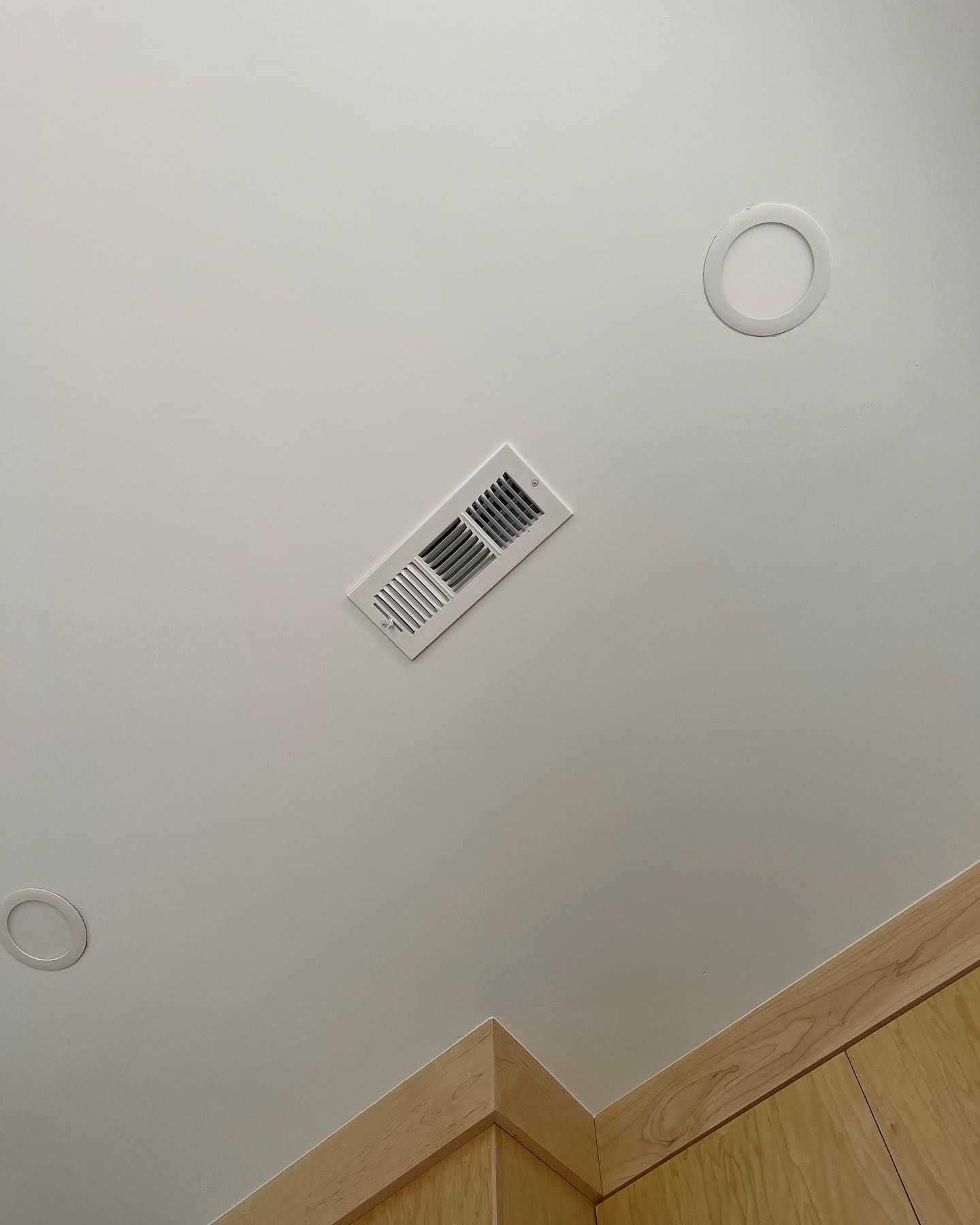 Ceiling with a white vent, recessed lighting, and a corner of a light wood cabinet.