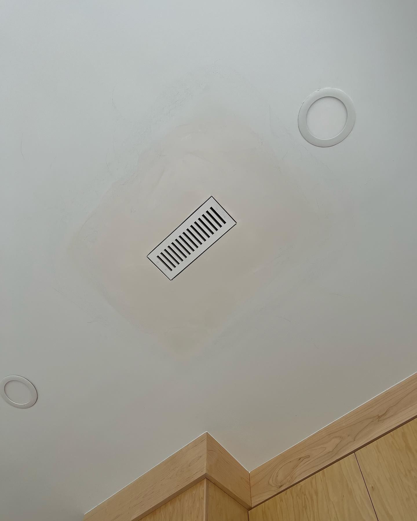 White ceiling with an air vent and two recessed lights. Light-colored cabinet in the corner.