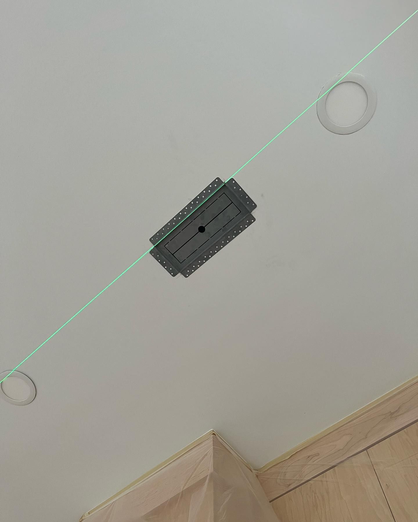 Green laser line on ceiling with a mounting bracket and recessed lighting.