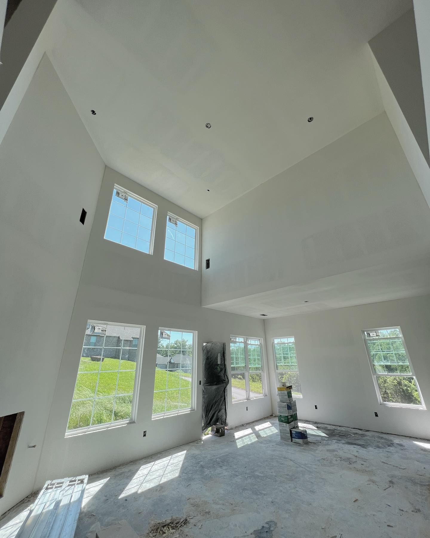 Interior view of a room with high ceilings, large windows, and unfinished walls and flooring.