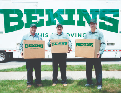 Three men holding boxes in front of a bekins moving truck.