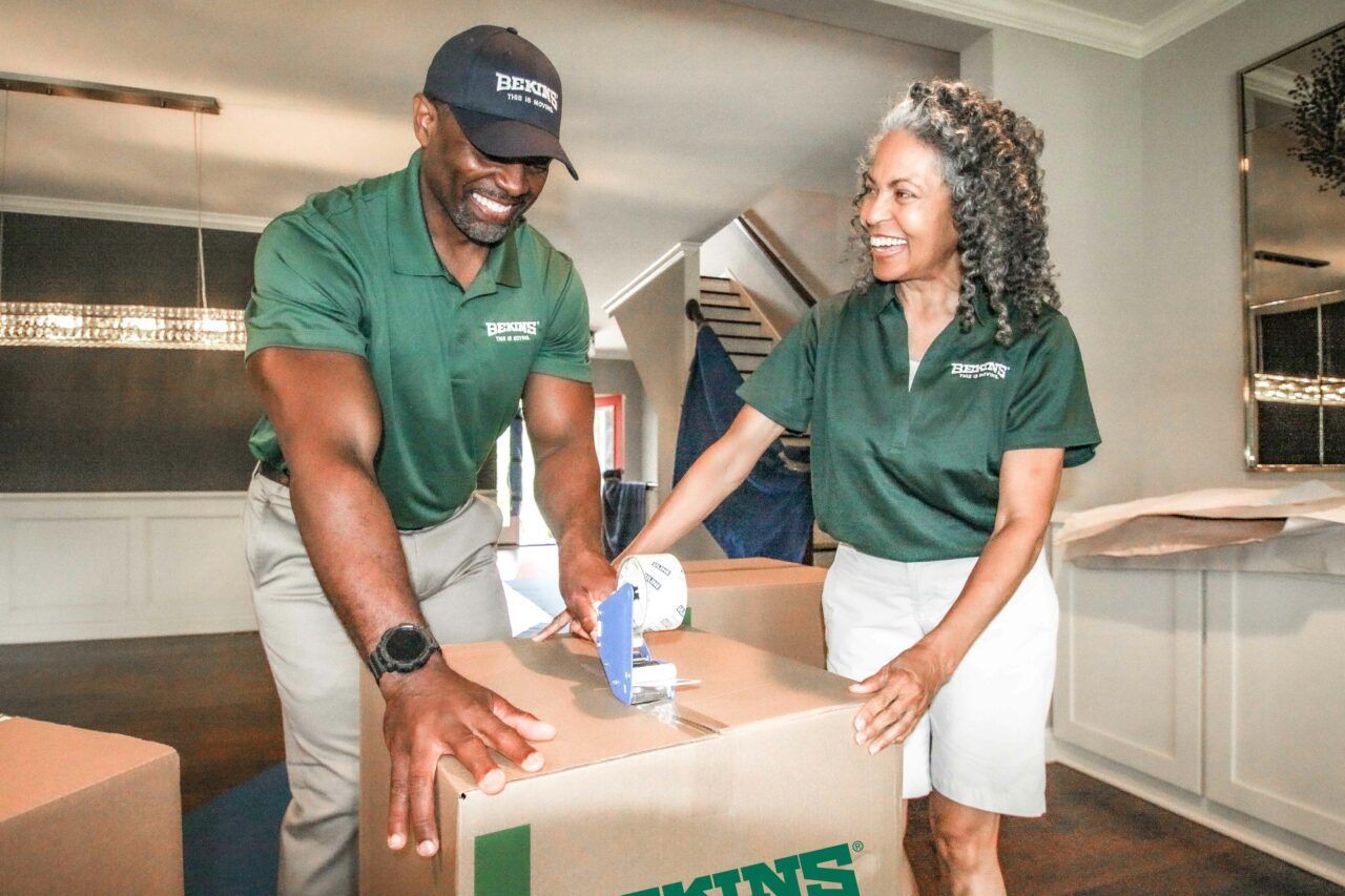 A man and a woman are packing boxes in a living room.