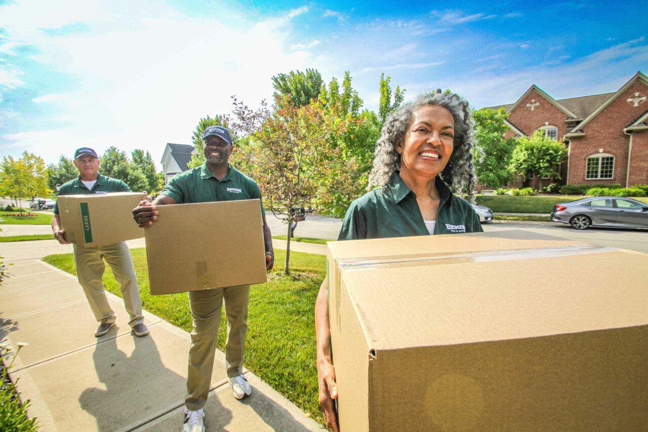 A group of people are carrying boxes down a sidewalk.