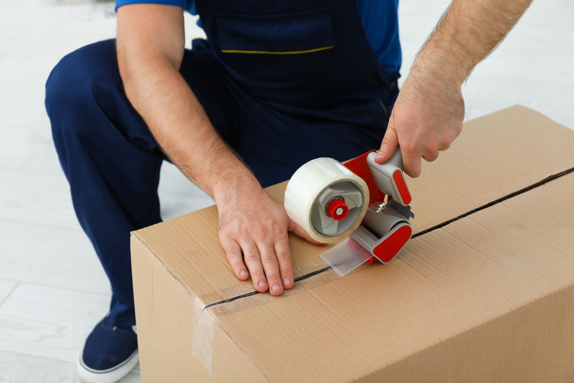A man is using a tape dispenser to seal a cardboard box.