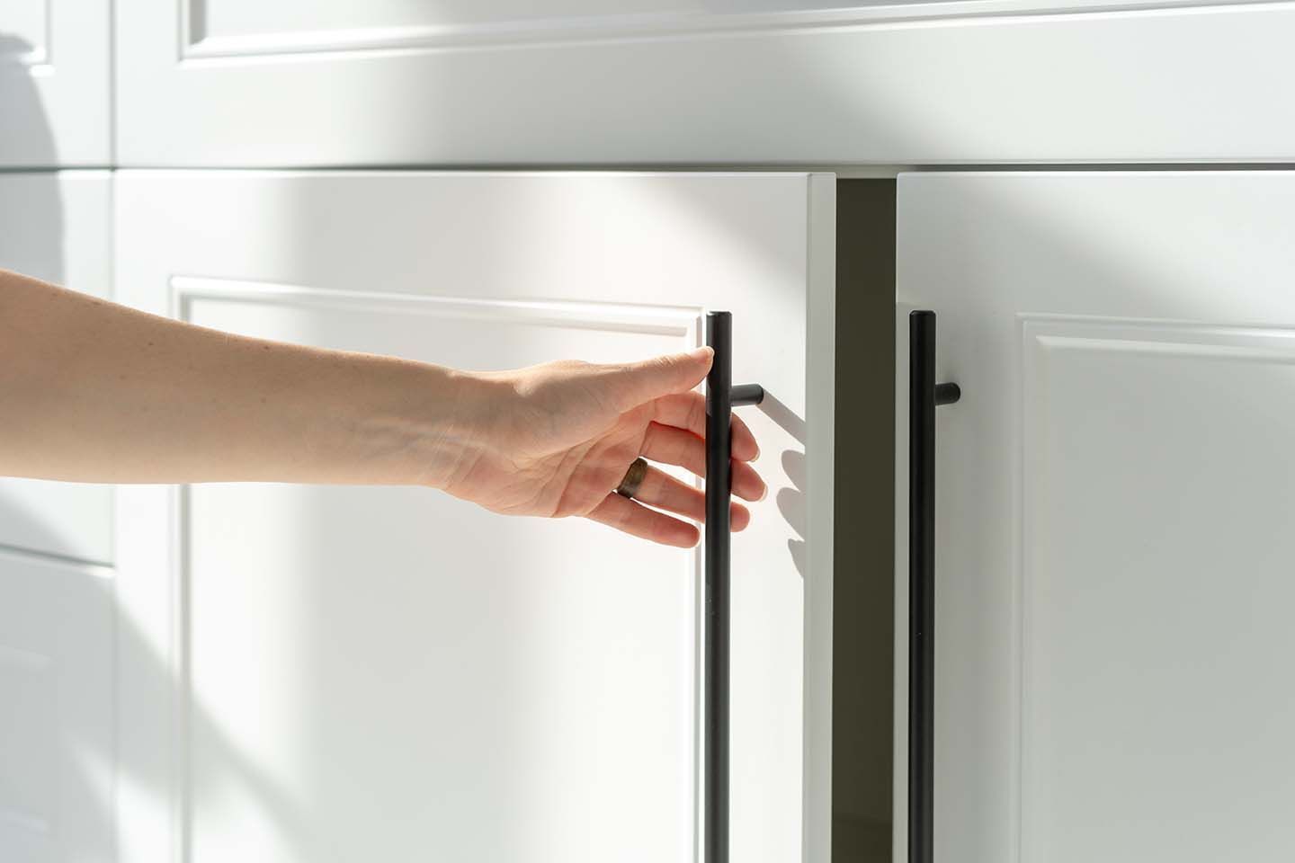 A person is opening a white cabinet with black handles.