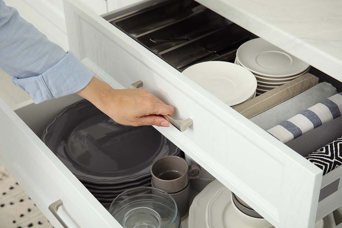 A person is opening a drawer filled with plates and cups.