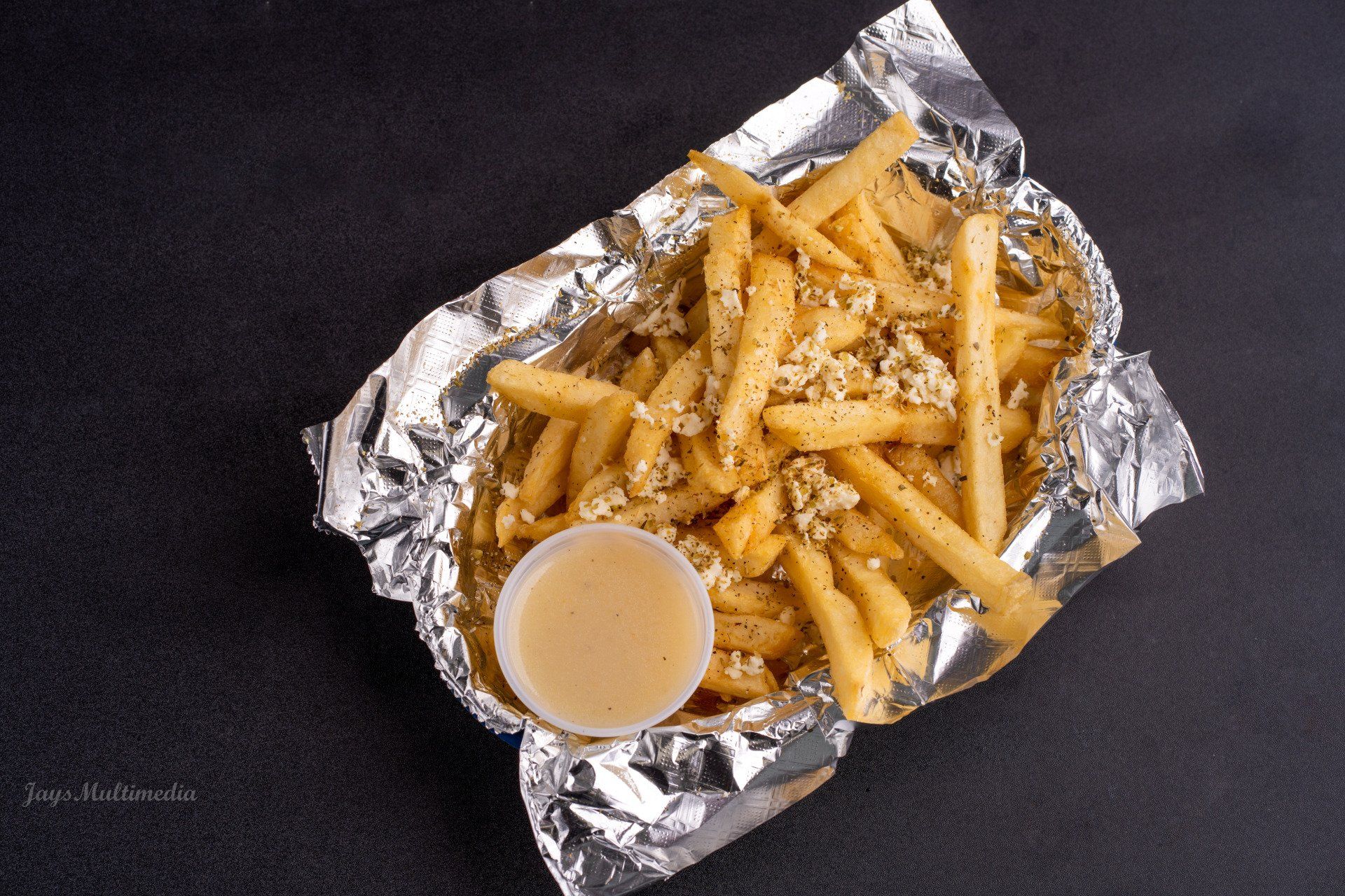 French fries are wrapped in tin foil with a small cup of dipping sauce.