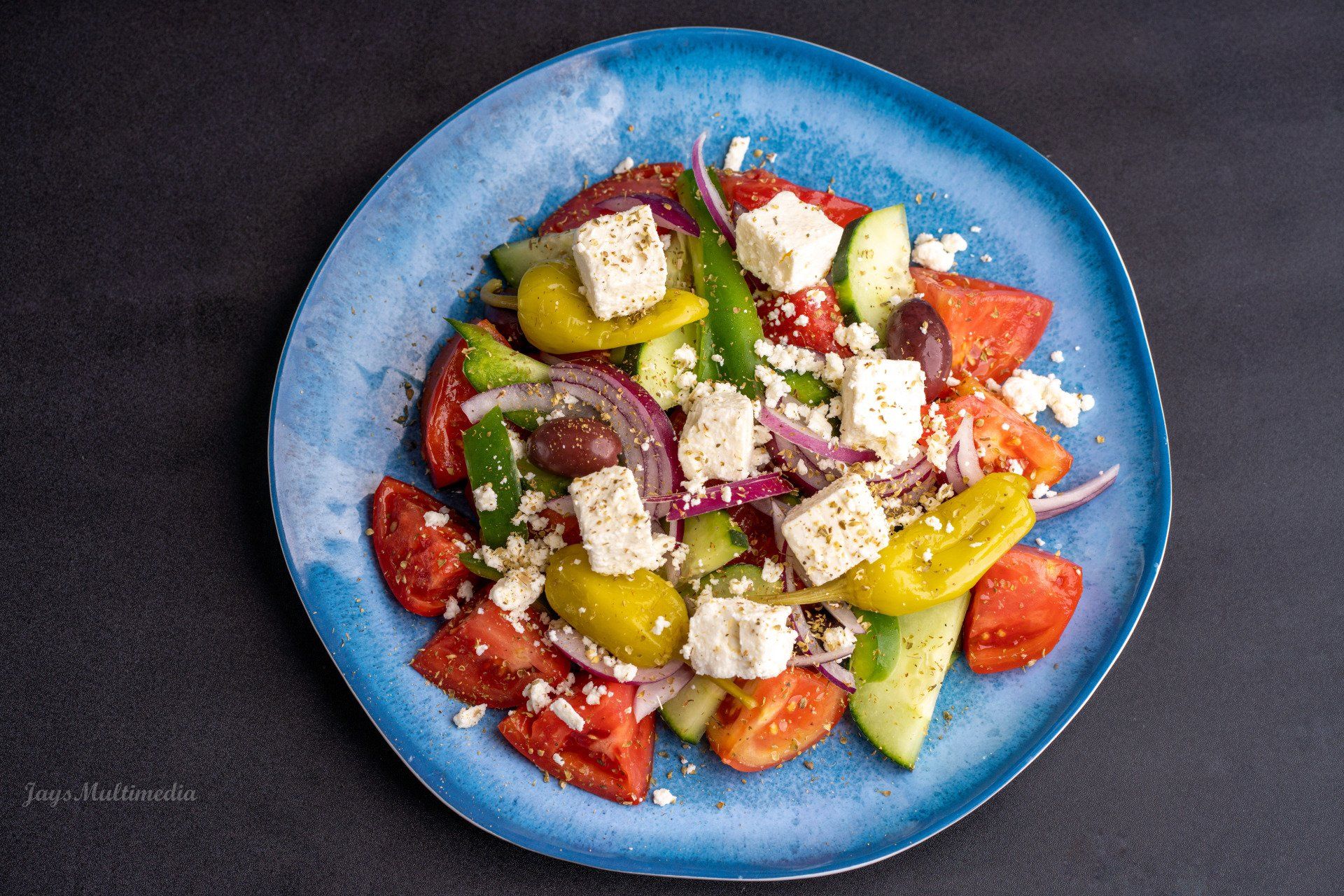 A blue plate topped with a salad of tomatoes , cucumbers , olives and feta cheese.