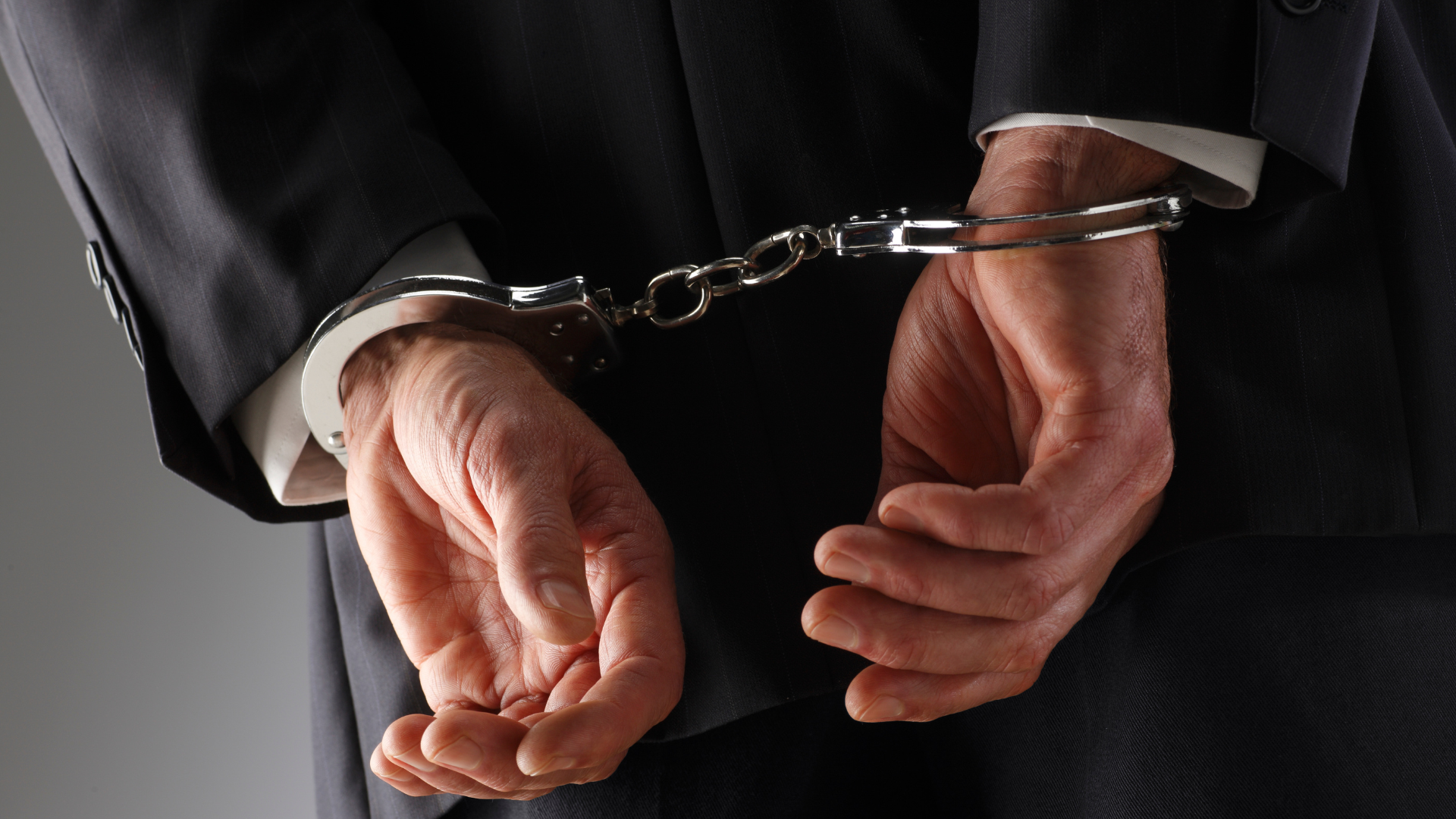 A man in a suit has his hands in handcuffs.