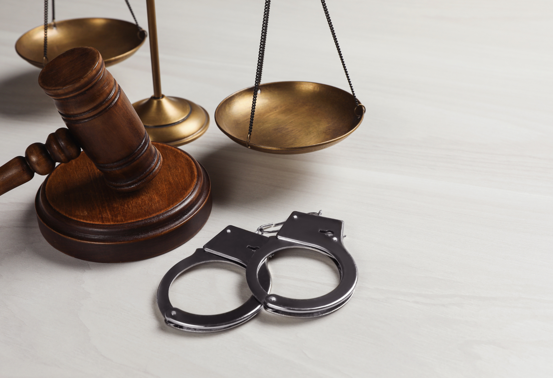 A pair of handcuffs sitting next to a judge 's gavel and scales of justice.