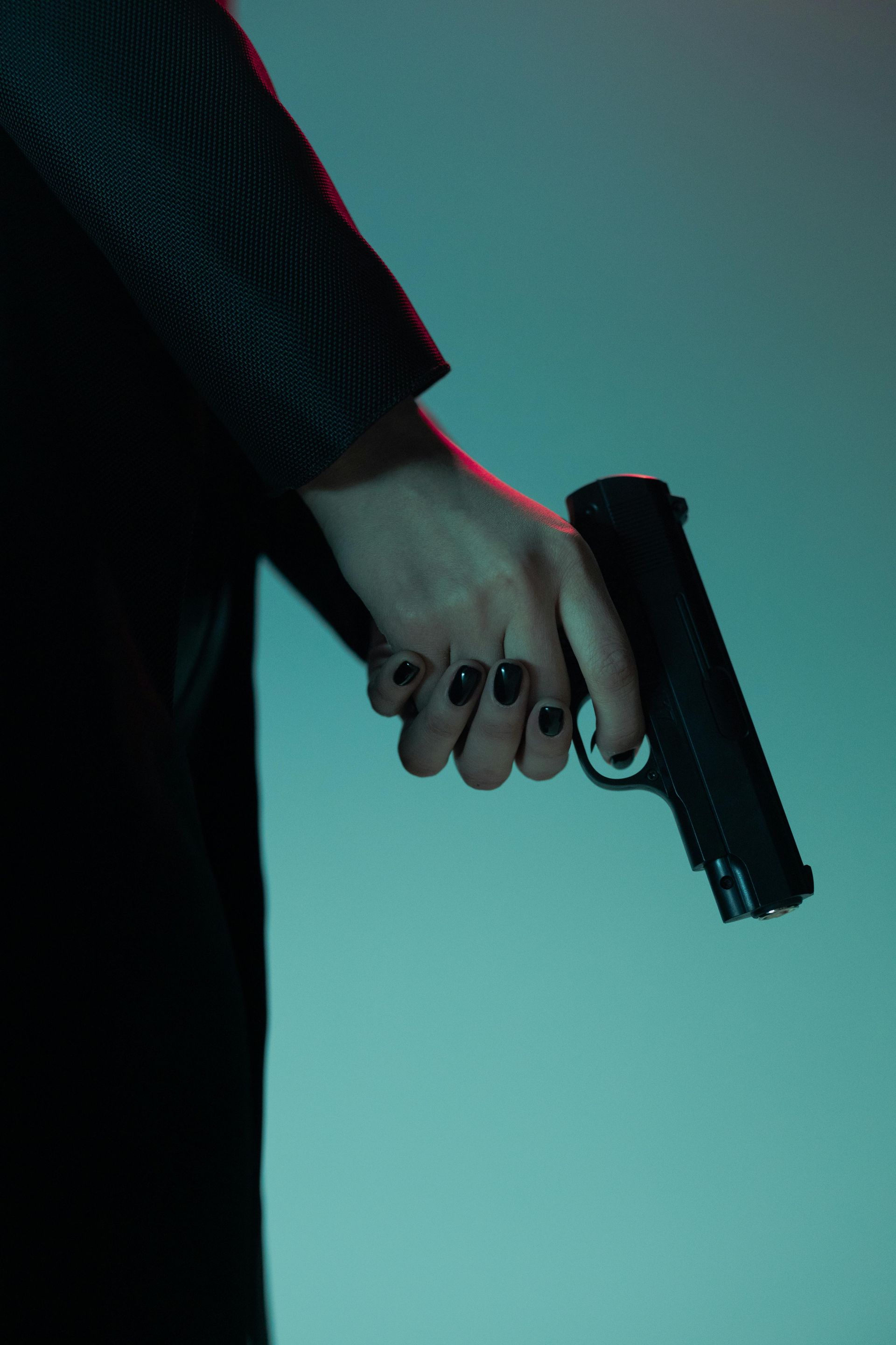 A hand with dark nail polish holds a black handgun, pointing slightly downward.