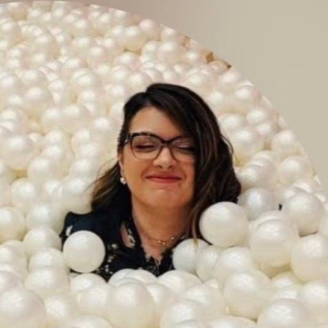 Woman with glasses smiling, immersed in a white ball pit.