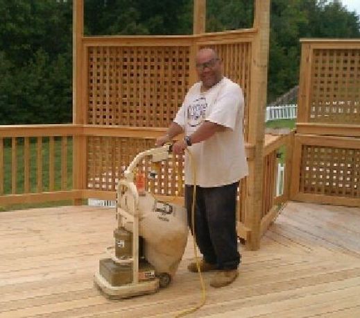 A man is sanding a wooden deck with a machine