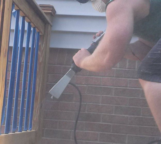 A man is cleaning a wooden railing with a high pressure washer