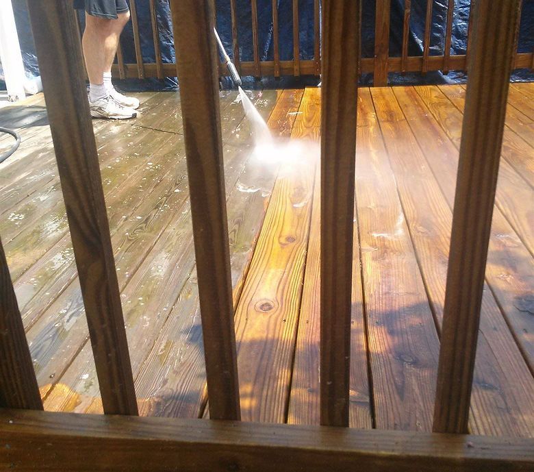 A person is cleaning a wooden deck with a high pressure washer