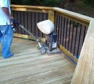 A man is using a machine to sand a wooden deck.