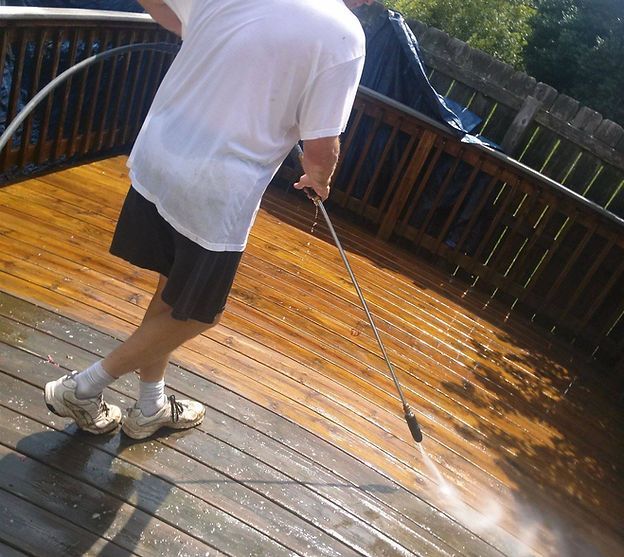 A man is using a high pressure washer to clean a wooden deck