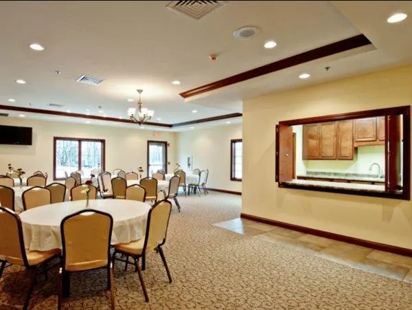 Banquet hall with round tables, tan chairs, and a serving window.
