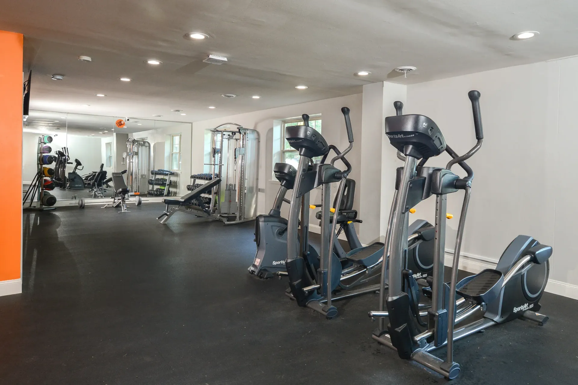 Indoor community gym featuring ellipticals, treadmills, and weight machines.