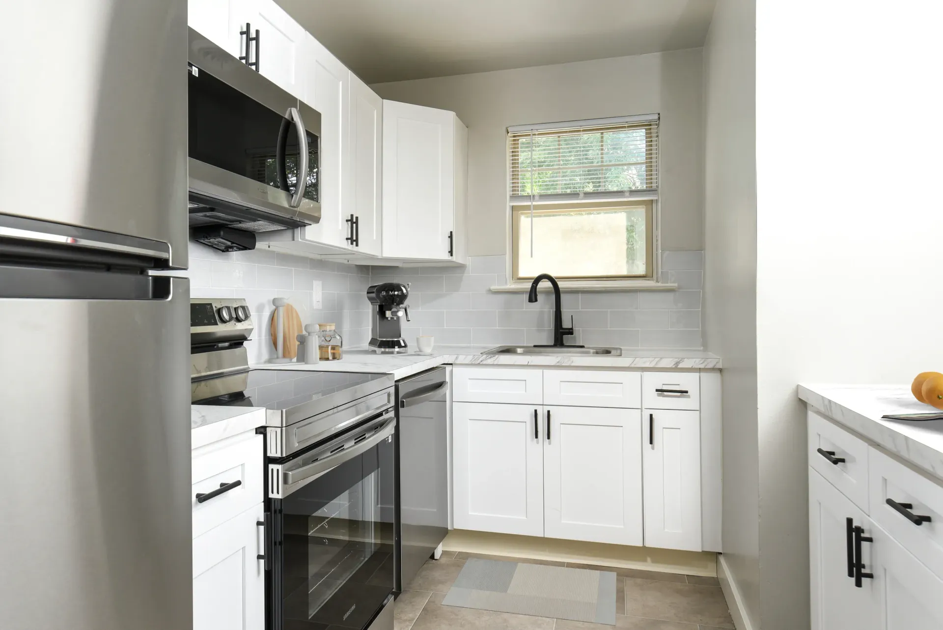 White kitchen with stainless-steel appliances, black faucet, and window above the sink.