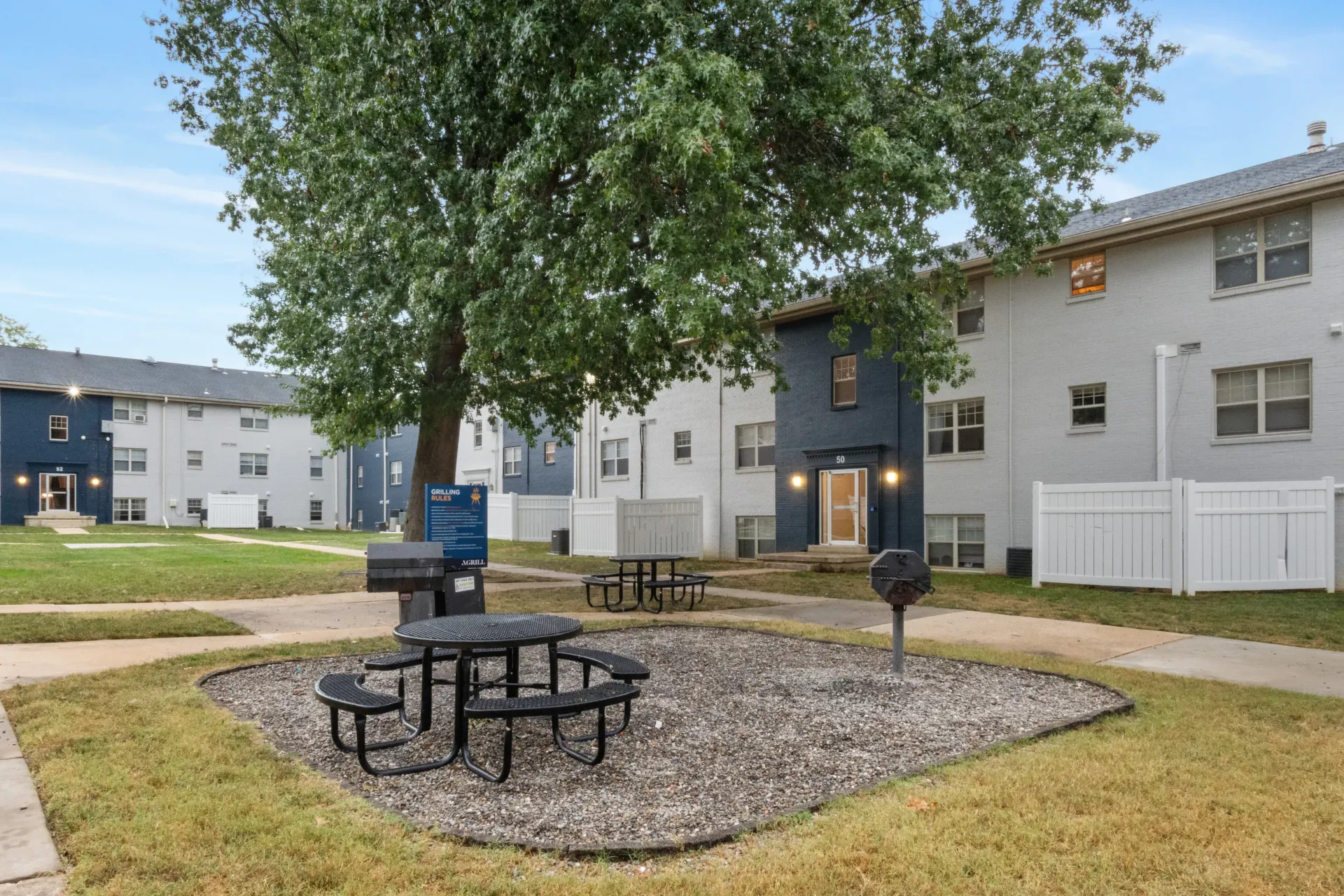 Outdoor community courtyard with picnic tables, a grill, and apartment buildings in the background.