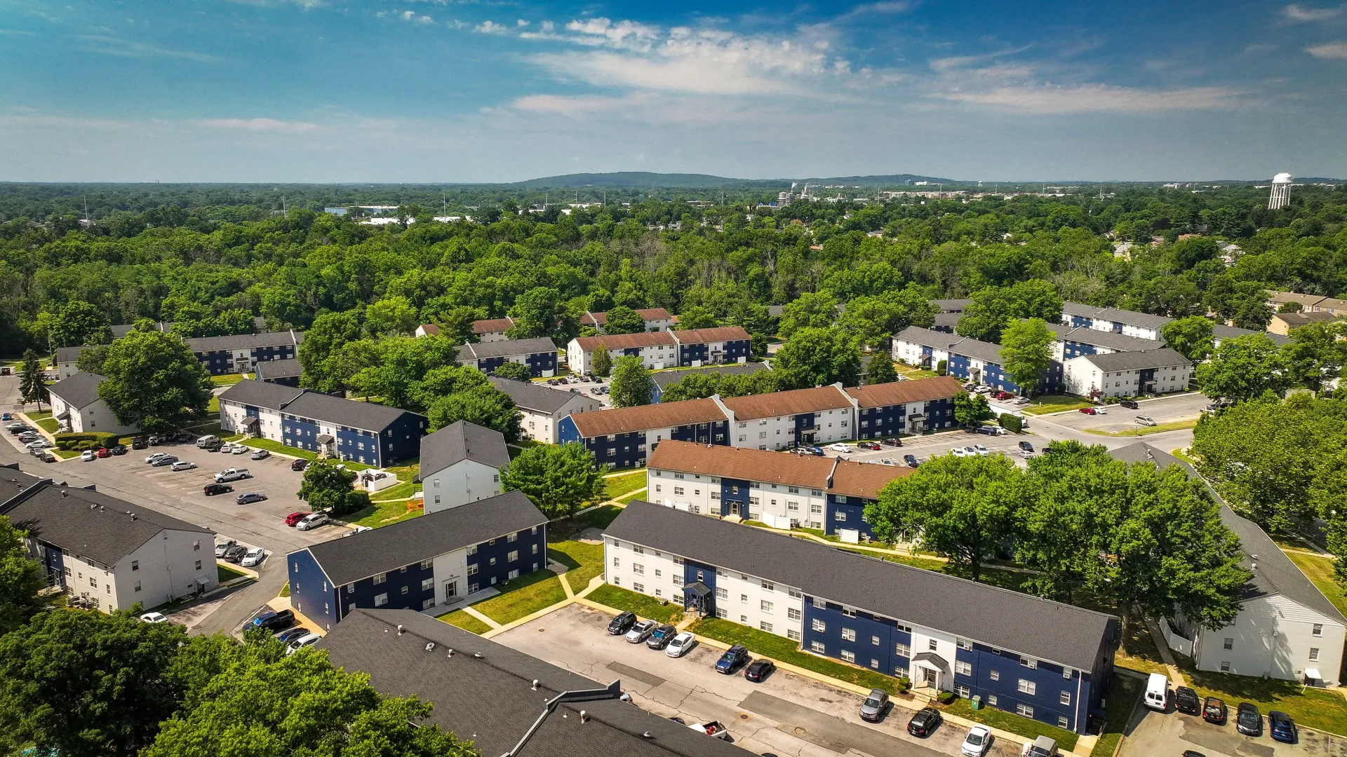 Aerial view of a multi-building apartment community with trees and parking.