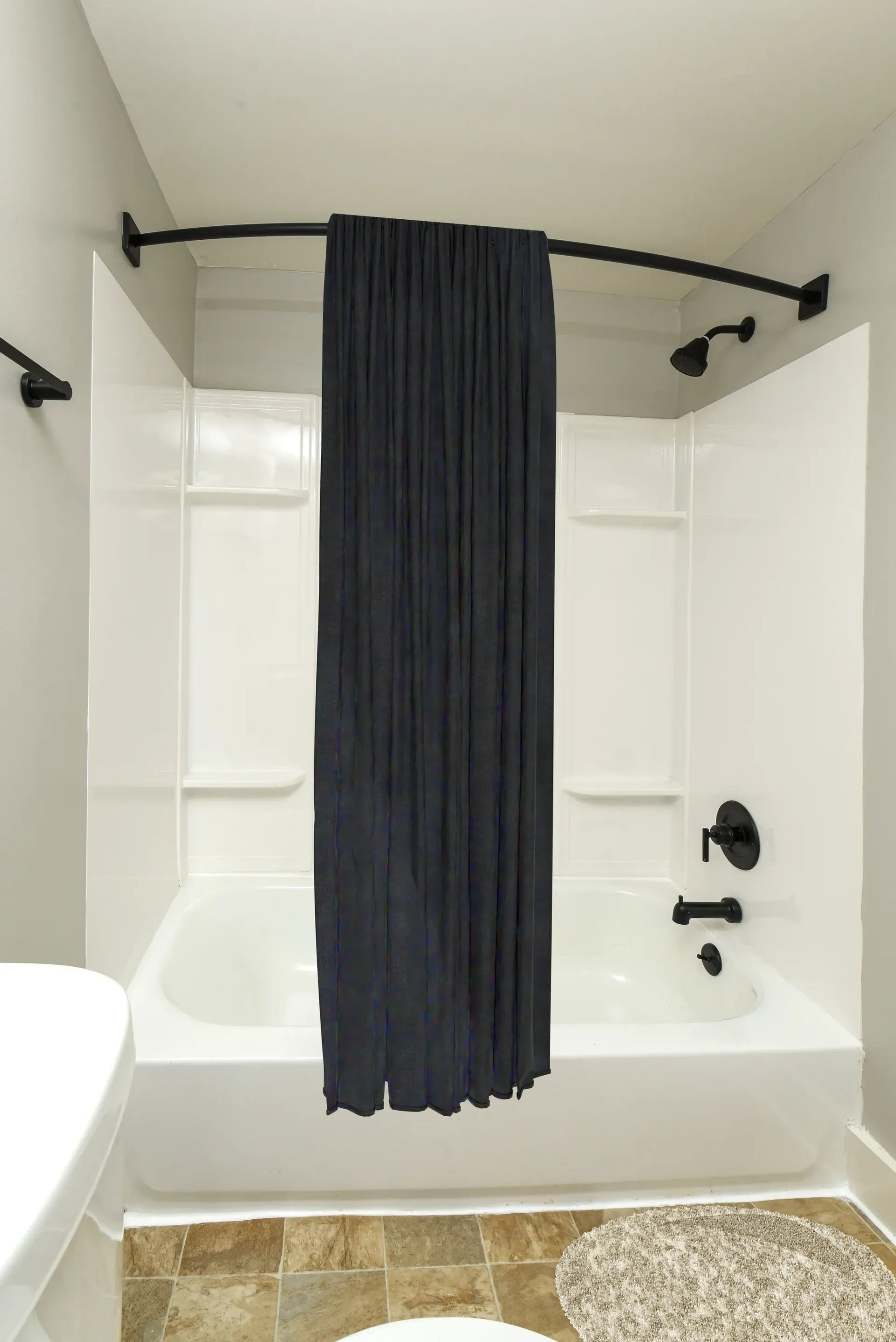 White bathtub with a dark shower curtain and black fixtures in a bathroom.