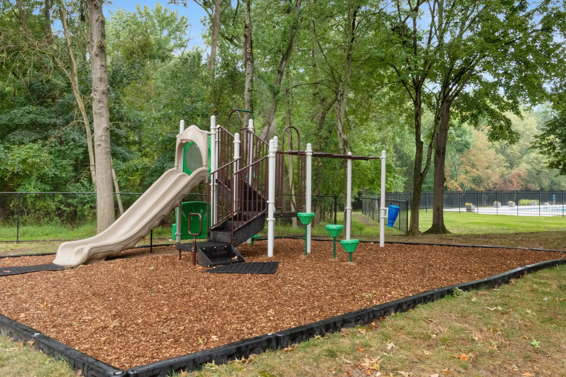 Tree-lined community playground with slide and climbing structure.