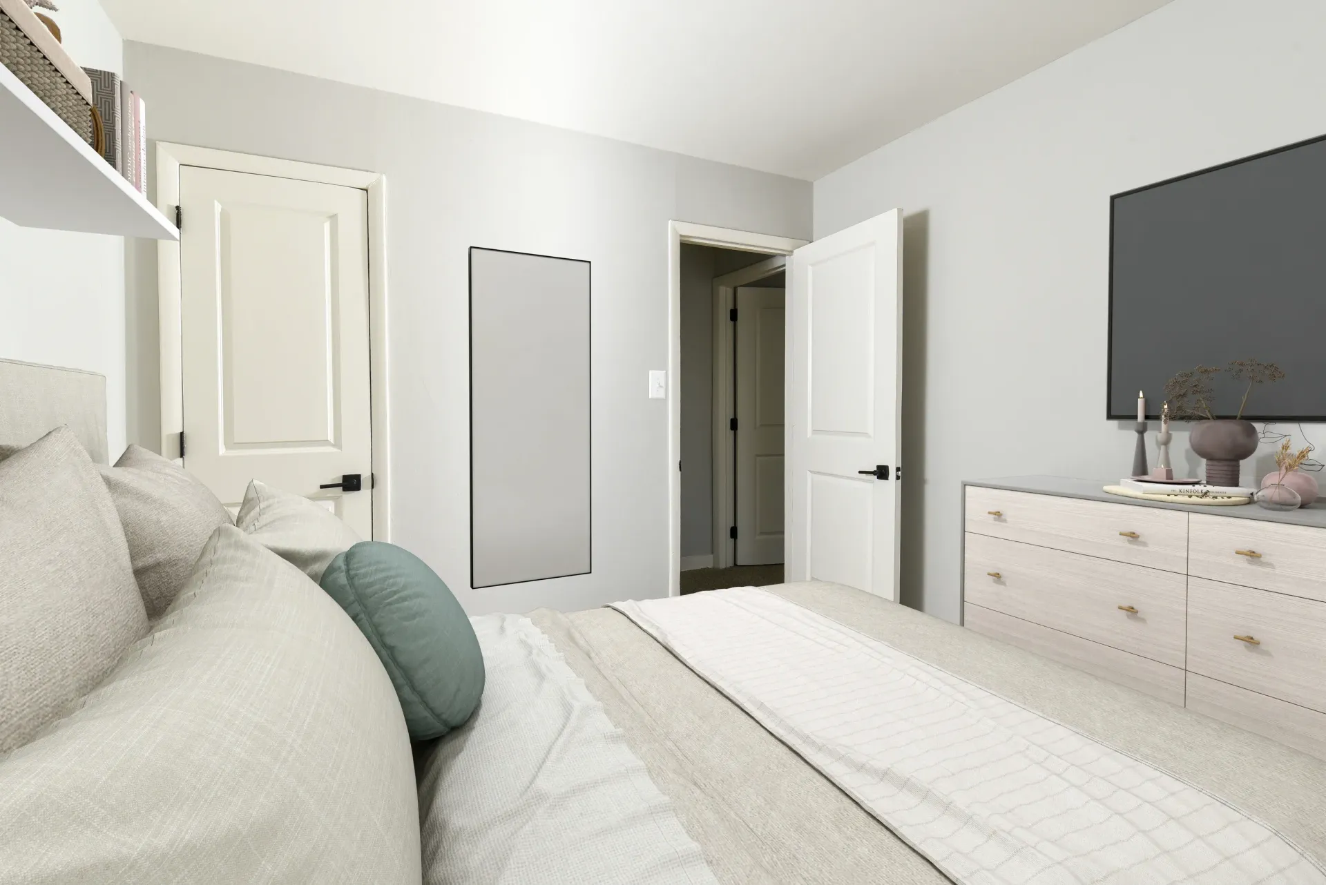 Modern bedroom with a neatly made bed, light grey walls, a dresser, and a wall-mounted TV.