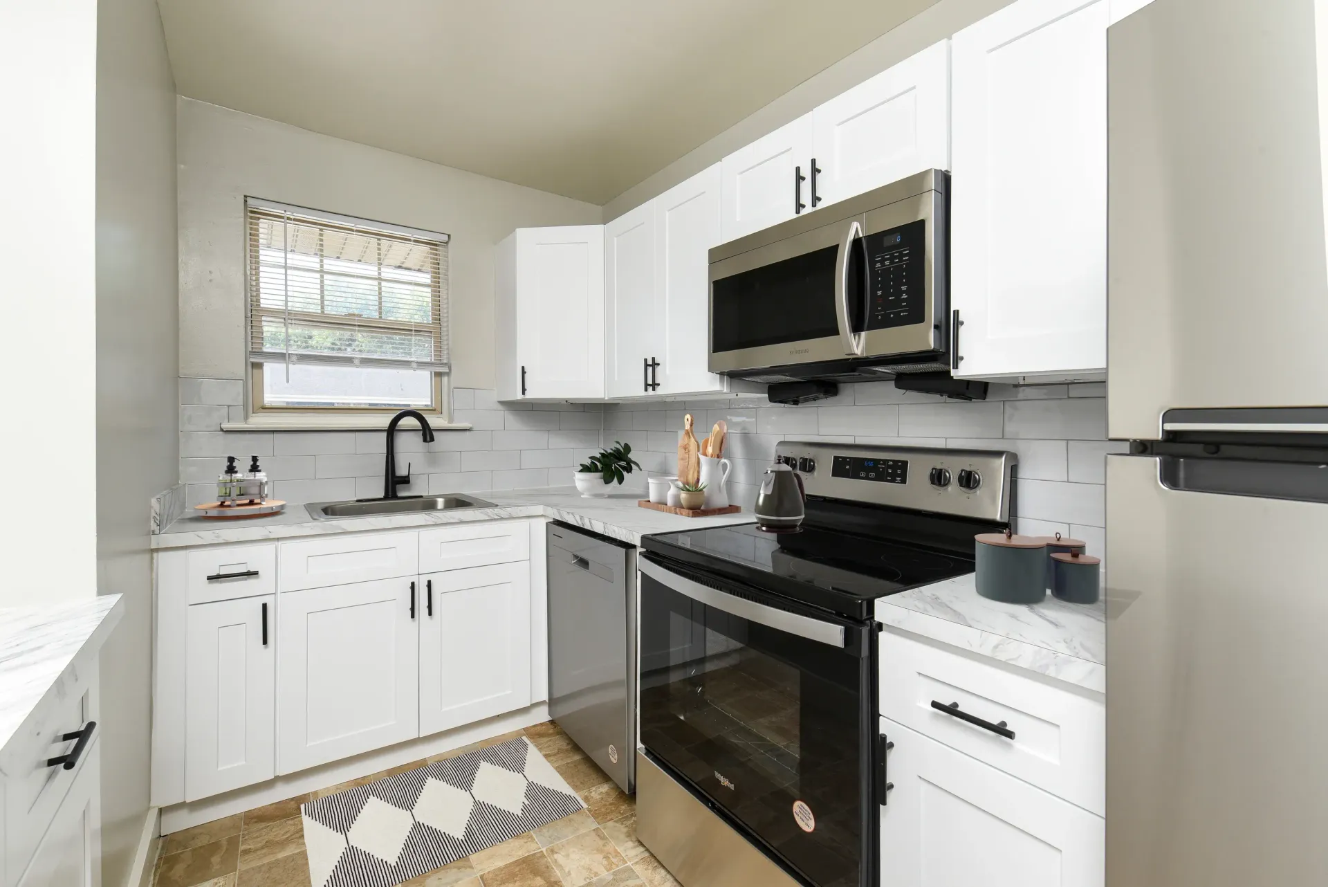 White kitchen with marble countertops, stainless appliances, and a window above the sink.