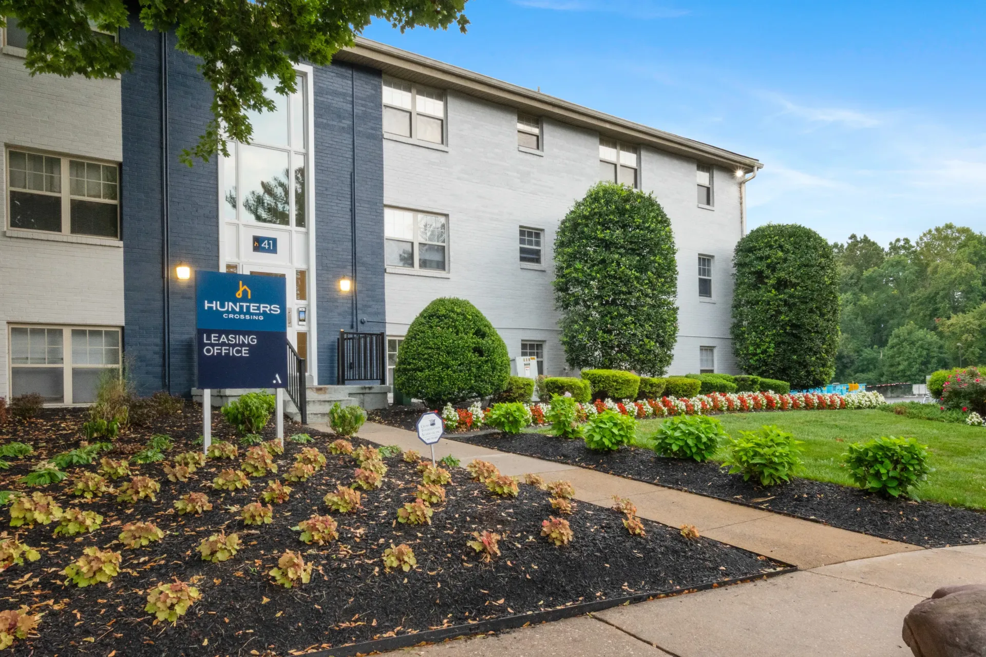 Exterior view of a multifamily building with manicured landscaping and a leasing office sign.