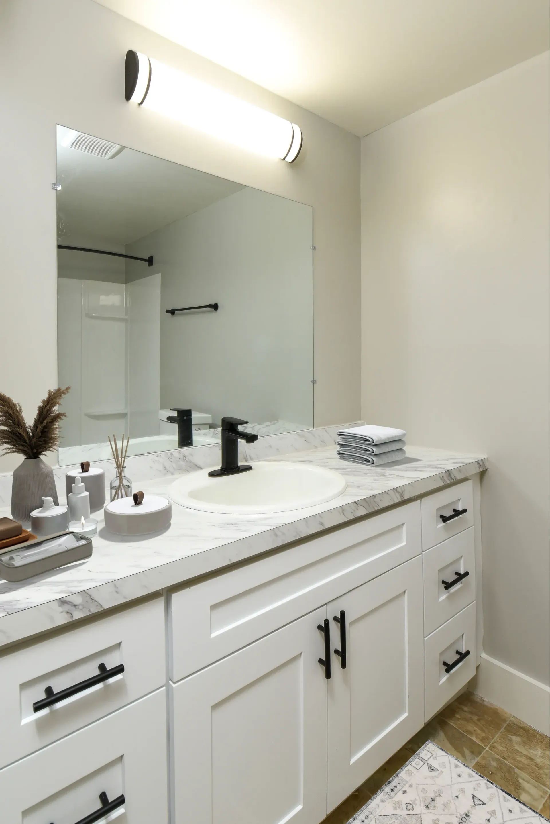 Bathroom vanity with marble countertop, black faucet, large mirror, and towels
