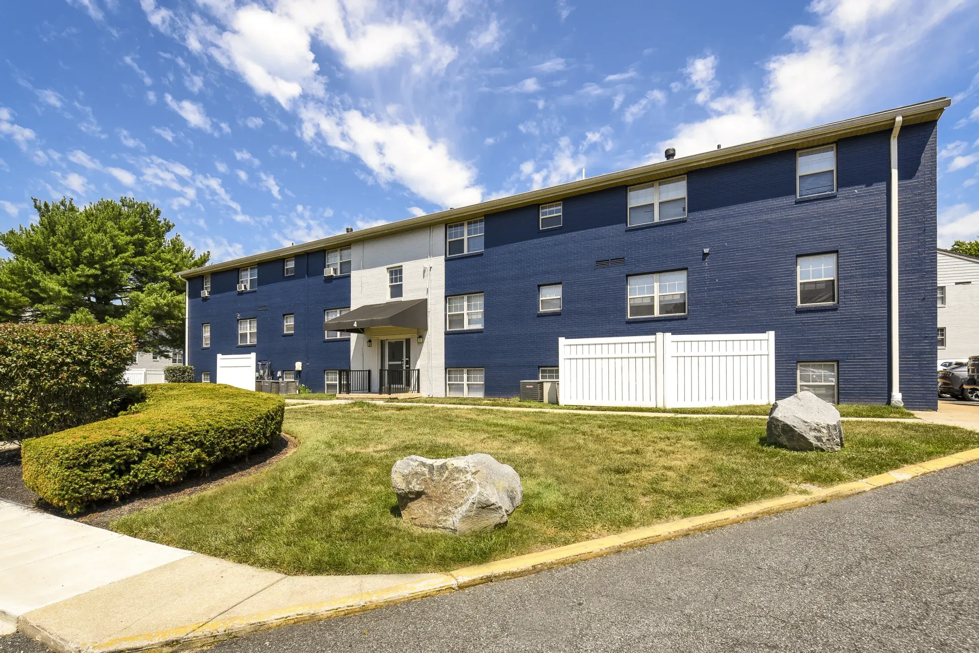 Exterior view of a blue brick apartment building with a small entry awning and landscaped lawn.