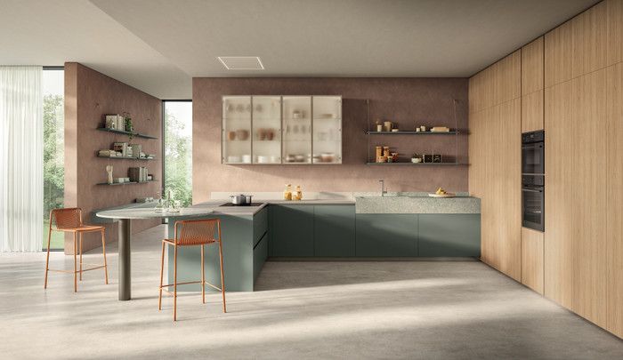 Una cucina moderna con mobili color verde salvia, pannelli in legno chiaro, pavimento in cemento e due sgabelli accanto al bancone per la colazione.