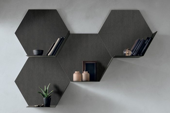 Mensole esagonali da parete moderne in legno scuro, disposte in modo sfalsato, che ospitano libri, una pianta e oggetti decorativi.
