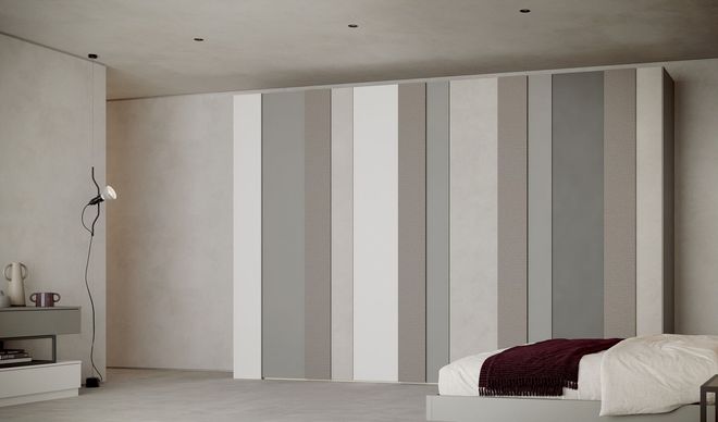 Una camera da letto moderna caratterizzata da un ampio armadio a tutta altezza con pannelli verticali in diverse tonalità di grigio, beige e bianco.