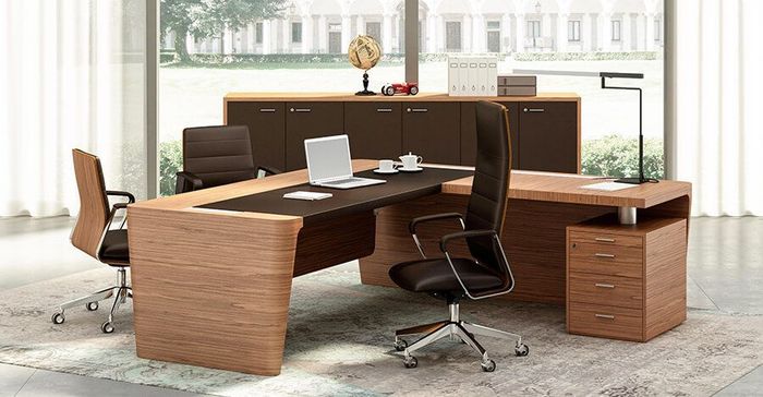 In una stanza luminosa, si trovano una moderna scrivania direzionale con intarsi in legno scuro, due sedie da ufficio in pelle e un mobile contenitore abbinato.