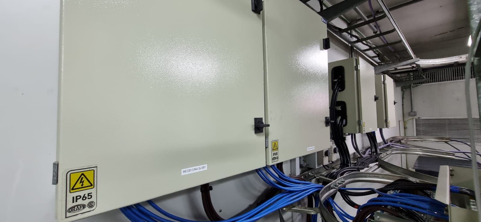 Armarios eléctricos industriales con cables azules en un pasillo de una sala de servidores.