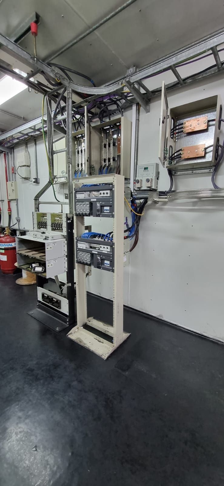 Paneles eléctricos industriales y conductos montados en la pared de un cuarto de servicio con suelo oscuro.