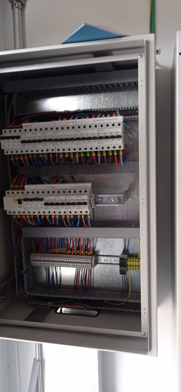 Armario de control eléctrico abierto con filas de disyuntores y cableado en su interior.