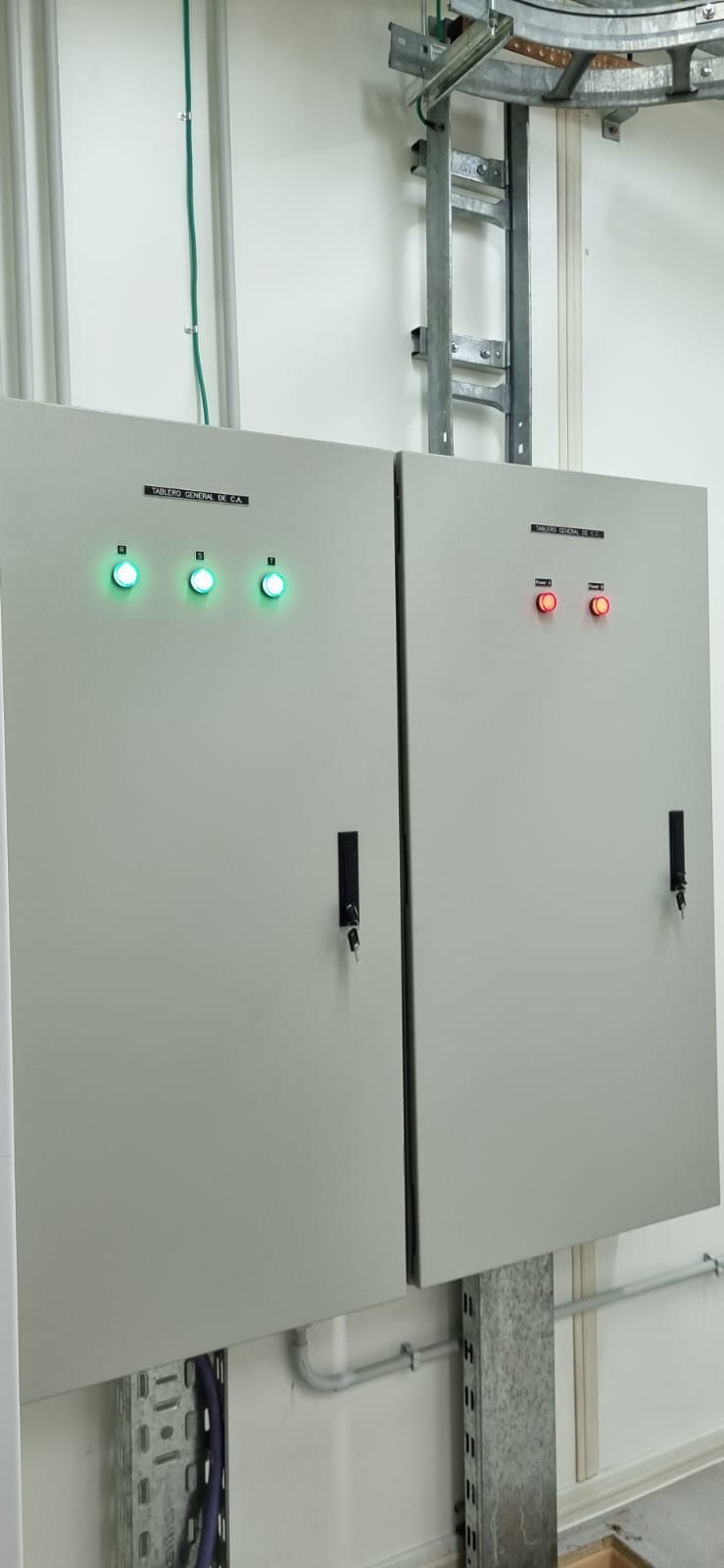 Dos armarios de control eléctrico grises con luces indicadoras verdes y rojas en un cuarto de servicio.