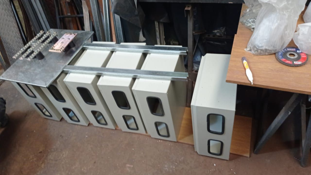 Una hilera de gabinetes de altavoces de color gris claro apilados en un taller, con una mesa pequeña y herramientas cerca.