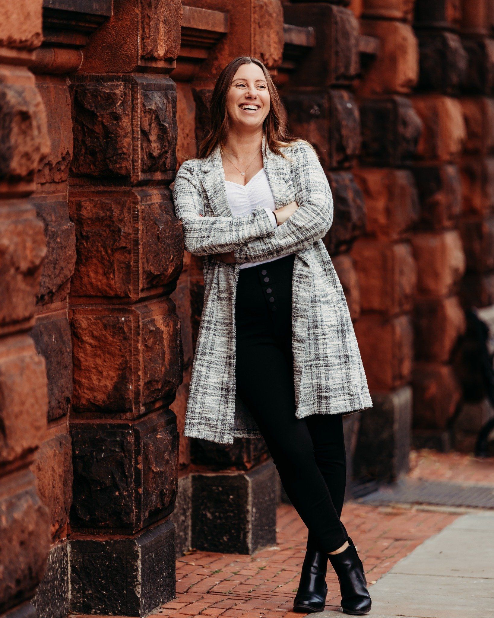 a woman is standing in front of a brick wall with her arms crossed and smiling .